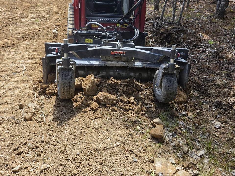 Skid steer with a power rake grading bare soil
